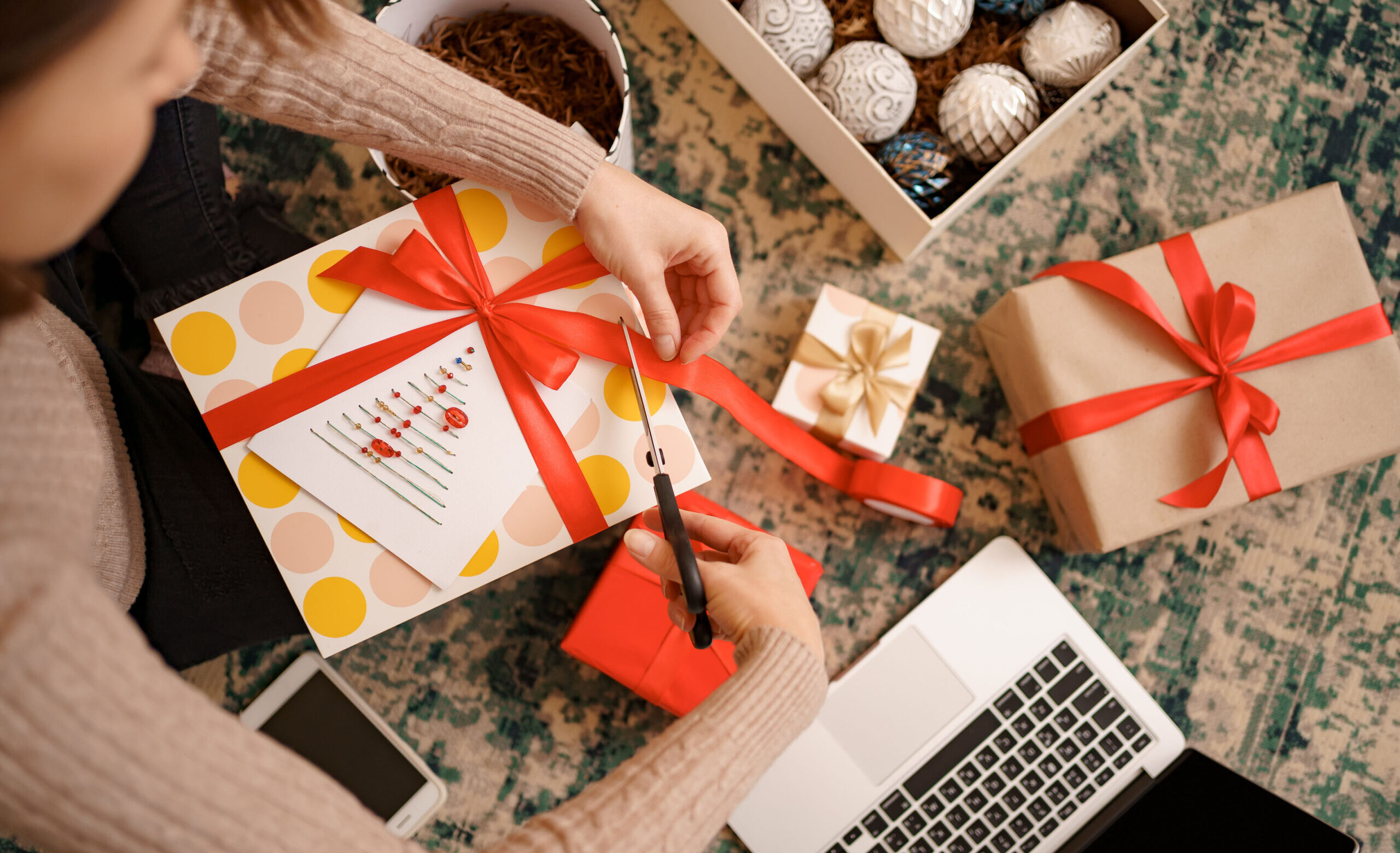 Woman wrapping Christmas gift while sitting on the carped in the living room